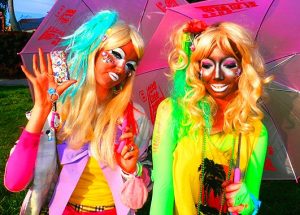 Image of two ganguro girls posing. Both these girl have very colorful hair color in neon green and yellow. Their make-up is also much more intense and darker.