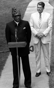 President Mobutu has on a leapord print traditional hat that points upwards in a triangularesque fashion. His Mao-like tunic is distinct for the collar, which looks like an elongated shirt-dress color attached to a coat. In contrast, President's suit is a traditional Western suit, worn with a collared dress shirt and complete with a tie. 