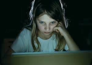 Young girl staring intently at a lit computer screen in a dark room