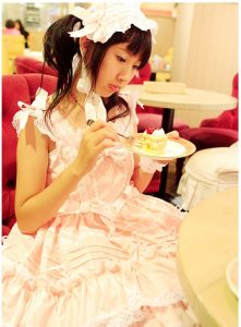 Japanese girl in Sweet Gothic Lolita with bonnet sits and eats cake.