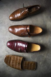 displays four types of the luxury crocodile shoes, which are made from crocodile skin and distinct for the scaly pattern. The styles and colors of the shoes vary, one being a maroon colored dress shoe, a brown sandal, and two types of bronze colored dress shoes. 