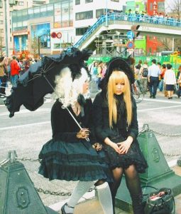 Two young Japanese women in Gothic Lolita with dresses, bonnets, wigs and parasols sitting in the street in Japan.