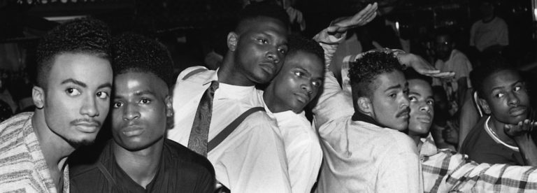 7 queer youth of color posing in a black and white photo. They are all wearing their street clothes. They are from the House of Jourdan.