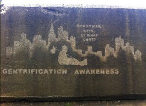 A reverse graffiti piece that reads "BEAUTIFUL CITY, AT WHAT COST? GENTRIFICATION AWARENESS"