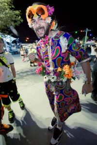 Raver at EDC 2012. He is wearing a colorful tunic and is covered in flowers and has some sort of orange furry hat on.
