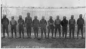 The British soccer team stands in front of a goal wearing gas masks during World War I