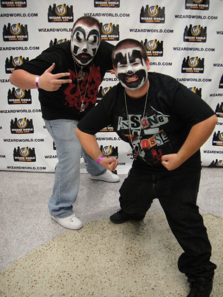 Two young Juggalos at an Insane Clown Posse gathering with clown makeup and ICP t-shirts standing in front of a backdrop.