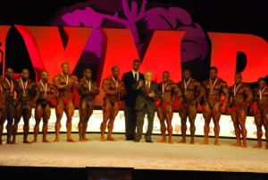 Bodybuilding competitors wearing medals lined up on the Mr. Olympia stage