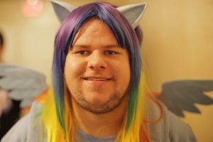 Photo of an adult male Brony in a rainbow wig, cat ears, and pony wings similar to the characters on the show.