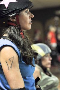 Roller derby participant with a star on her helmet and the number 17 on her arm looks to the right.
