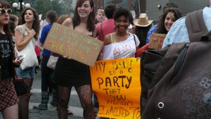 Two women marching in a Women's March holding anti-rape signs with the crowd in the background.