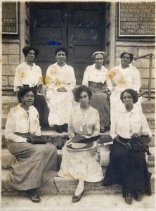 A black and white image of African American women sitting on the steps up to a building.