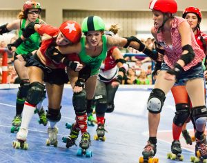 Skaters wearing green and red uniforms attempt to block and pass one another.