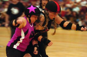In the midst of a roller derby bout, one skater goes to shoulder block the opposing team's jammer.
