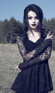 A goth woman stands with arms crossed, presumably outdoors