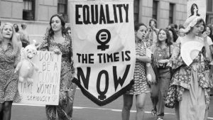 Black and white photo of women holding a banner that says "equality the time is now"
