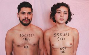 A man and woman, shown topless with "society says ok" written on the man's chest and "society says not ok" on the woman's chest